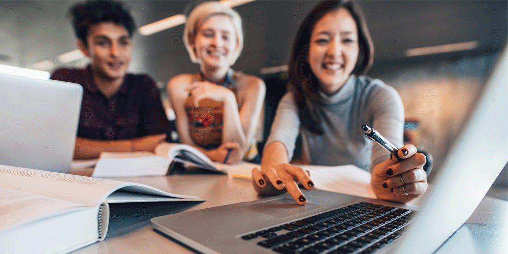 Three young workers sitting together looking at the same laptop.